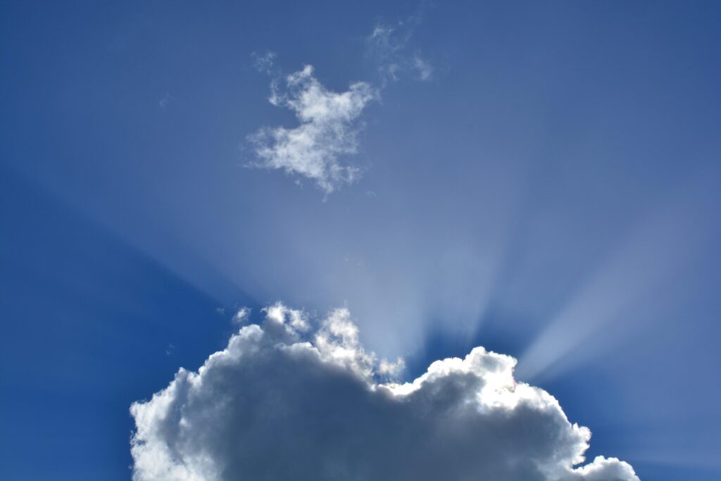Dramatic scene of sun rays shining through clouds against a vivid blue sky.